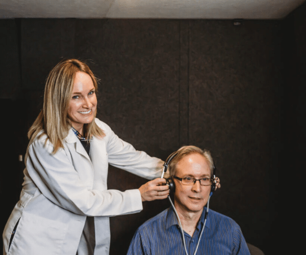 Female Audiologist performing a hearing exam inside of a WhisperRoom audiometric booth.