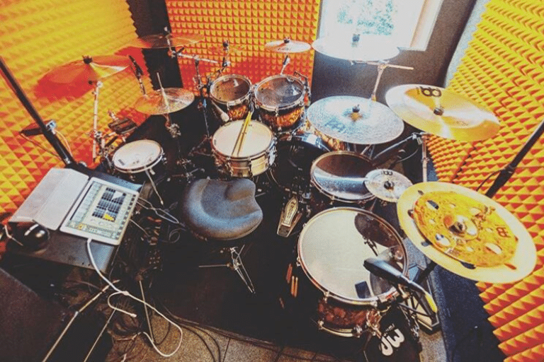 Full drum kit inside a WhisperRoom practice room with closed door and orange acoustic foam lining the walls.