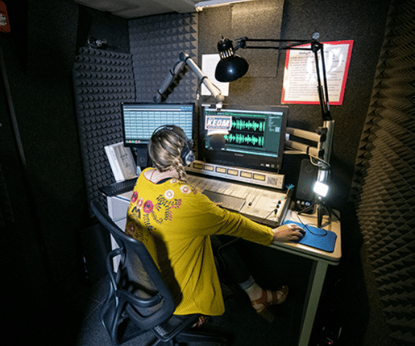 A young woman recording a radio broadcast inside of a WhisperRoom broadcast booth.