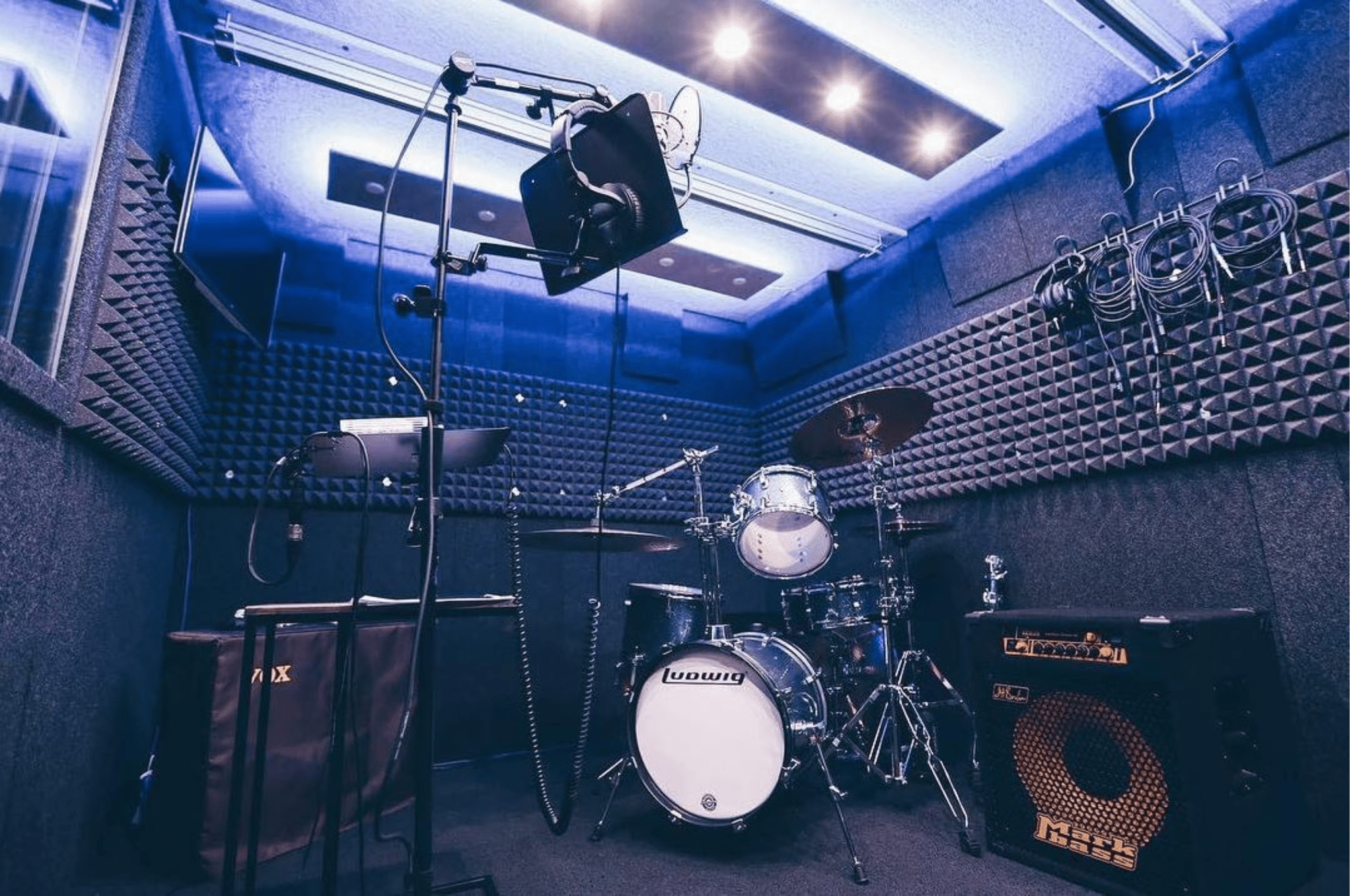 Interior of a WhisperRoom Practice Room showcasing a full drum kit, bass amp, guitar amp, monitor, microphones, and other musical gear for practice.