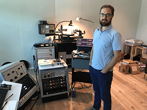 Mastering engineer Ryan Smith standing next to a collection of audio gear