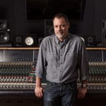Recording producer Steve Genewick leaning on his mixing console in a studio