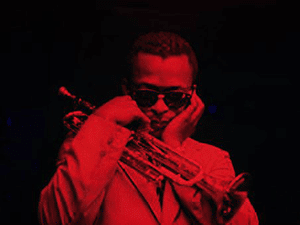 Miles Davis plugging his ears while holding a trumpet