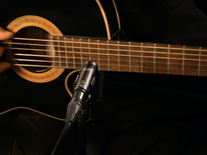 A black acoustic guitar and a microphone for recording