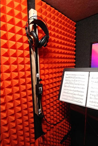 A music stand, orange foam, and headphones inside of a WhisperRoom MDL 4896 E.