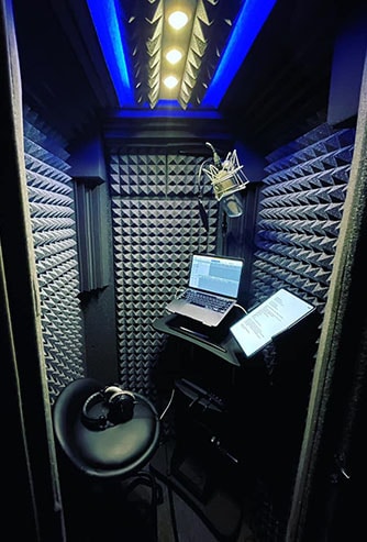 The interior of WhisperRoom's Voice Over Basic Package shown with a computer, microphone, headphones, and chair.