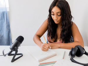 Woman writing a plan for her podcast with microphone and headphones on the table