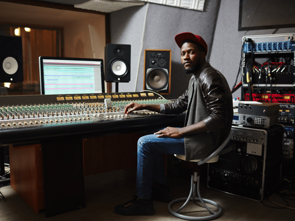 A music producer sitting at a mixing table in a recording studio during a session.