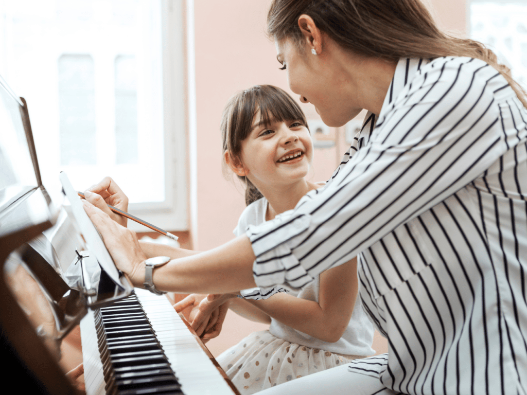 A mother playing piano with her daughter during a lesson.