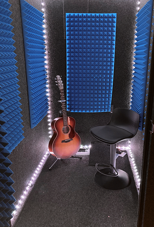 An acoustic guitar and a chair inside a WhisperRoom MDL 4872 S with blue foam on the walls.