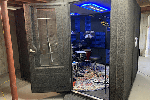 A WhisperRoom MDL 96120 S with a drum set and overhead mics set up inside of a home's basement.
