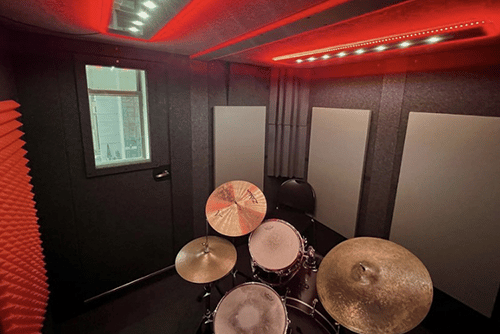 An interior photo of Michiko Studios WhisperRoom Drum Booth Package with a drum set, acoustic treatment, and red studio lights.
