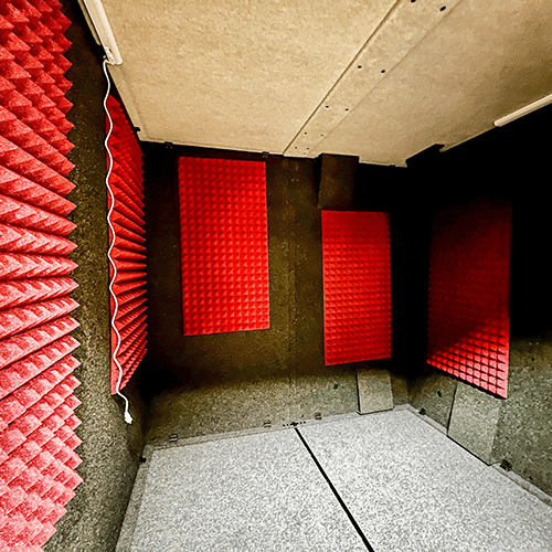 An interior photo of a WhisperRoom MDL 8484 S soundproof booth with orange acoustic studio foam on the walls.