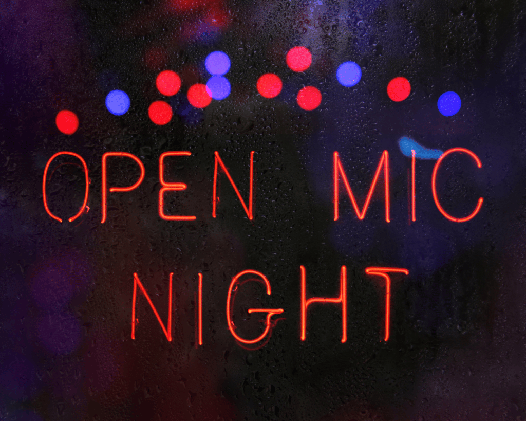 An image of a neon sign in a window that says "open mic night".