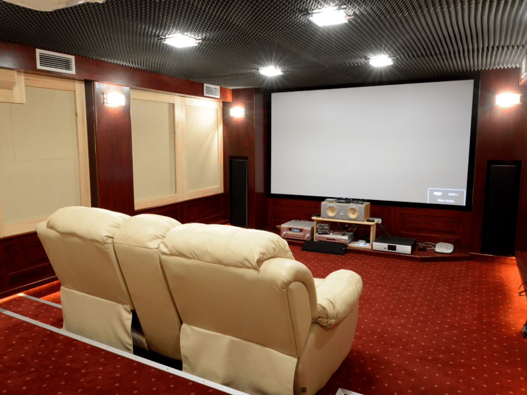 A home theatre inside of a soundproofed space inside of a home. Showing two recliners, red carpet, and a projector/screen.