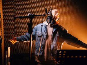 Image of a man wearing headphones and singing into a microphone at a recording studio.