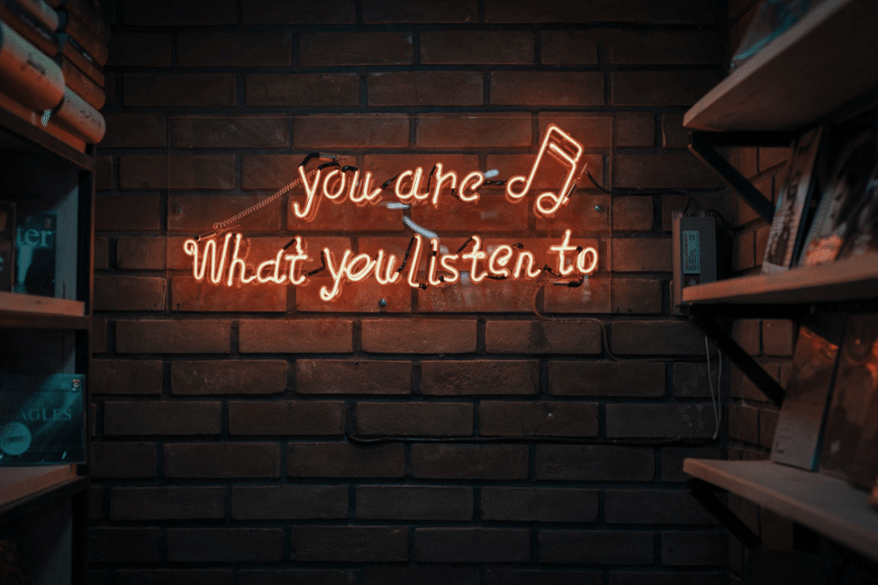 An image of a brick wall featuring a vibrant neon sign that reads 'you are what you listen to.' The sign is illuminated with bright colors, creating a visually striking display.
