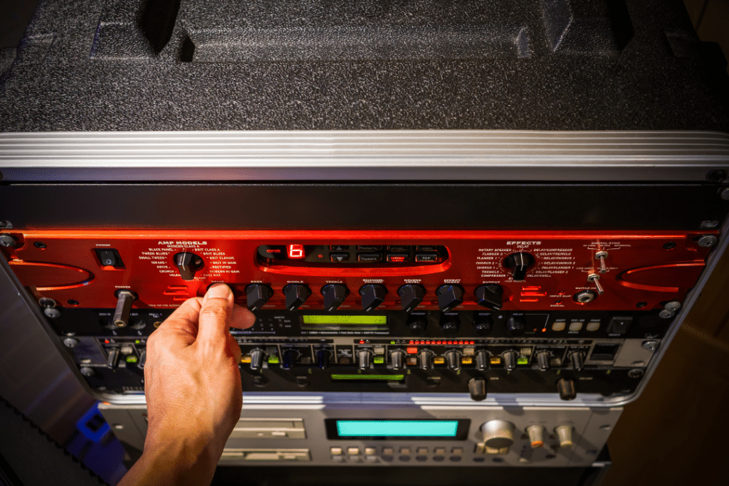 A hand adjusting the gain knob on a preamp/mixer stack. The hand is positioned near the control panel, precisely adjusting the gain knob to control the input signal level. This action helps optimize the audio signal and minimize unwanted noise or distortion in the recording or mixing process.
