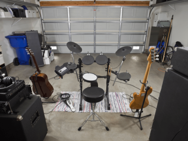 An inviting garage studio setup featuring a drum set in the center, flanked by a bass and a guitar on stands, showcasing a practical and personal space for music creation, symbolizing the theme of the blog post 'Rock Solid Silence - The Art of Garage Studio Soundproofing'