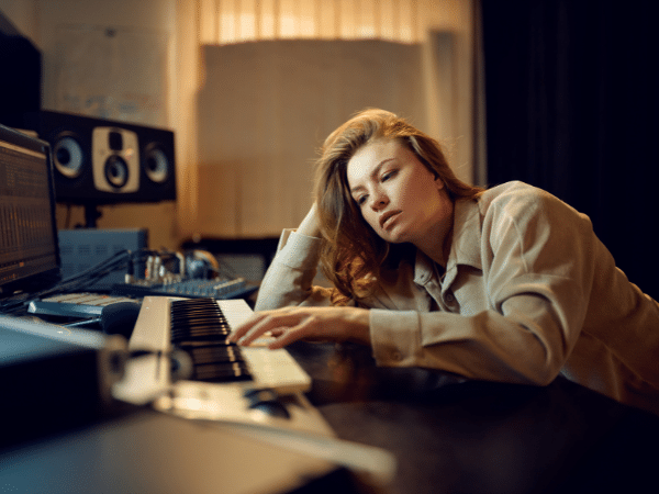 Woman experiencing studio fatigue, sitting at a keyboard looking exhausted during a recording session.