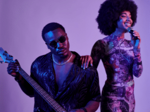 Close-up of a male bass player and female vocalist, featured in an article about building a personal brand as a musician, showcasing their dynamic as a musical duo under ambient purple lighting.